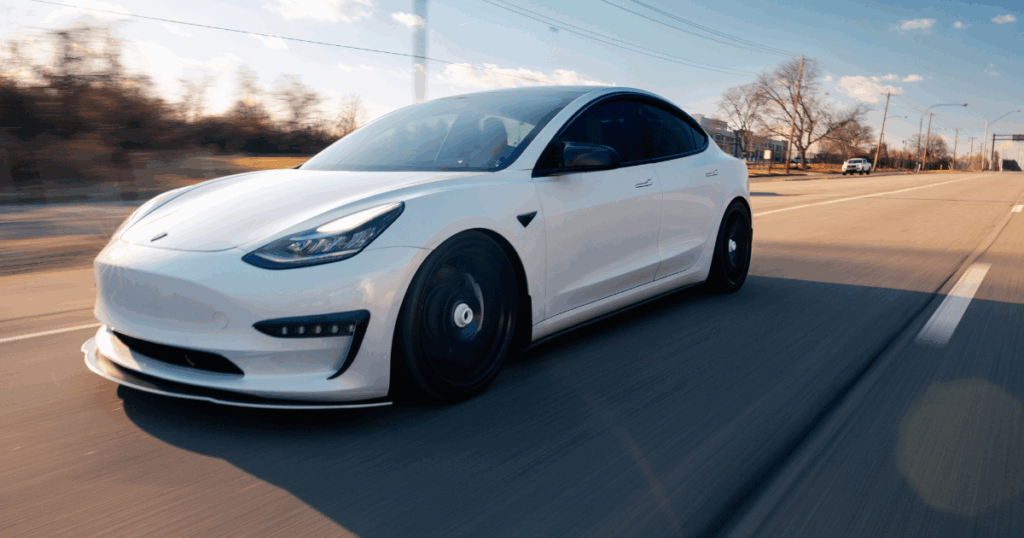 White Tesla electric vehicle driving on a scenic road in Australia