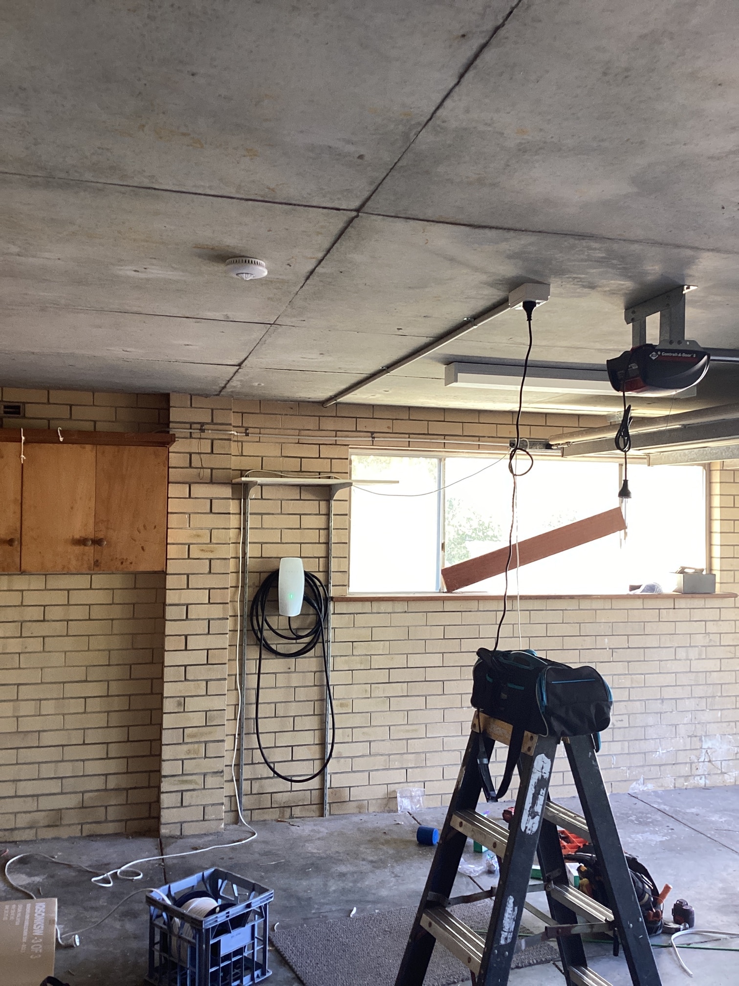 Emerald ceiling-mounted heat detector installed in a residential garage alongside a Tesla Wall Connector EV charger