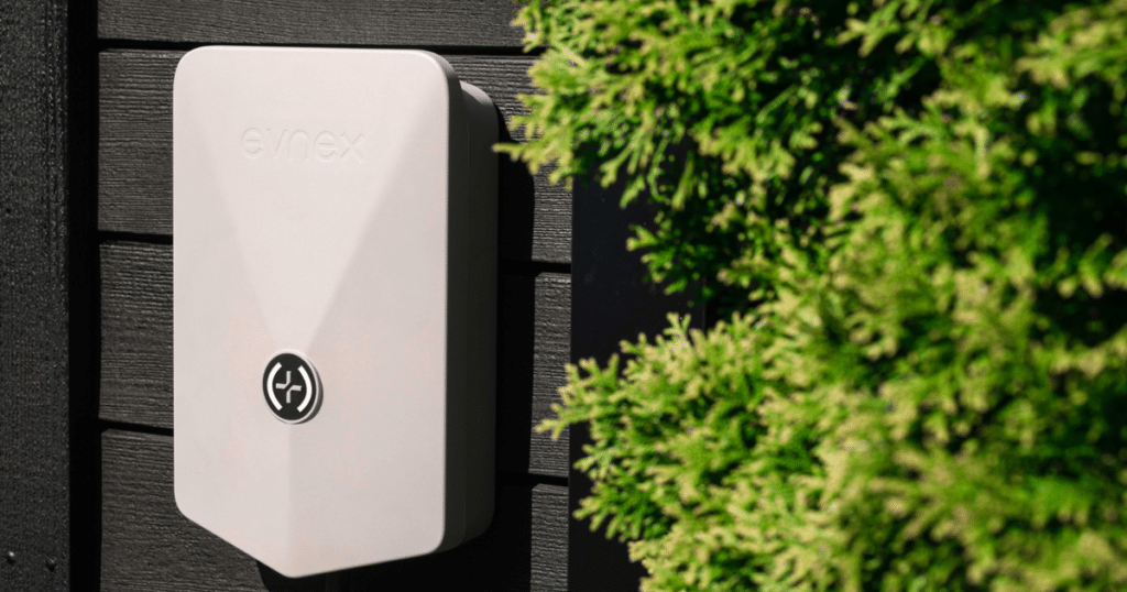 Evnex EV charger mounted on black timber wall with green garden backdrop.
