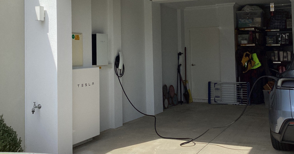 EV charger installation Perth featuring a Tesla Wall Connector and Powerwall battery mounted in a home garage, charging an EV
